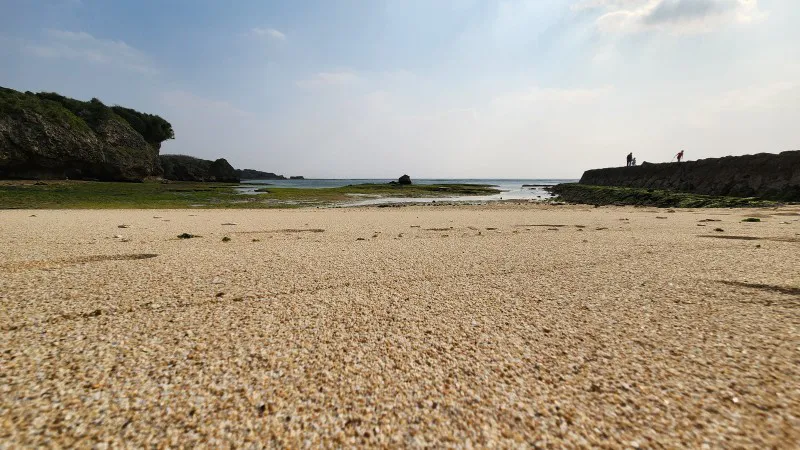 Sandy beach with rocky cliffs and tidal pools at Yomitan Coral Farm in Okinawa