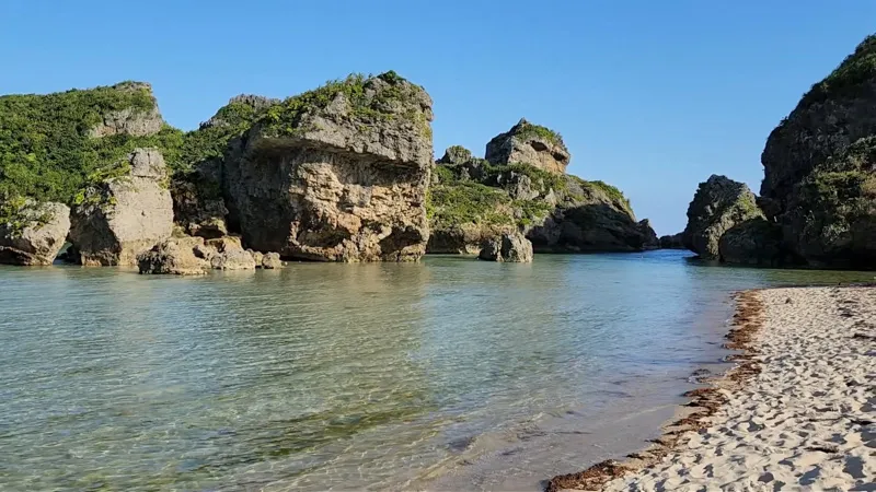 Plage de sable blanc avec de grandes formations rocheuses dans une eau bleue cristalline à Hamahigajima