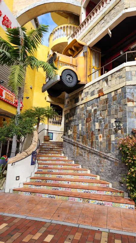 Colorful tiled staircase with a suspended yellow truck at American Village Okinawa