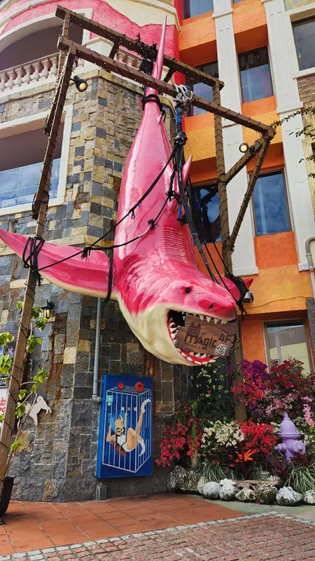 Large pink shark sculpture hanging outside a building at American Village Okinawa