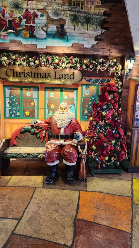 Santa Claus sitting on a bench next to a decorated Christmas tree at Christmas Land Okinawa