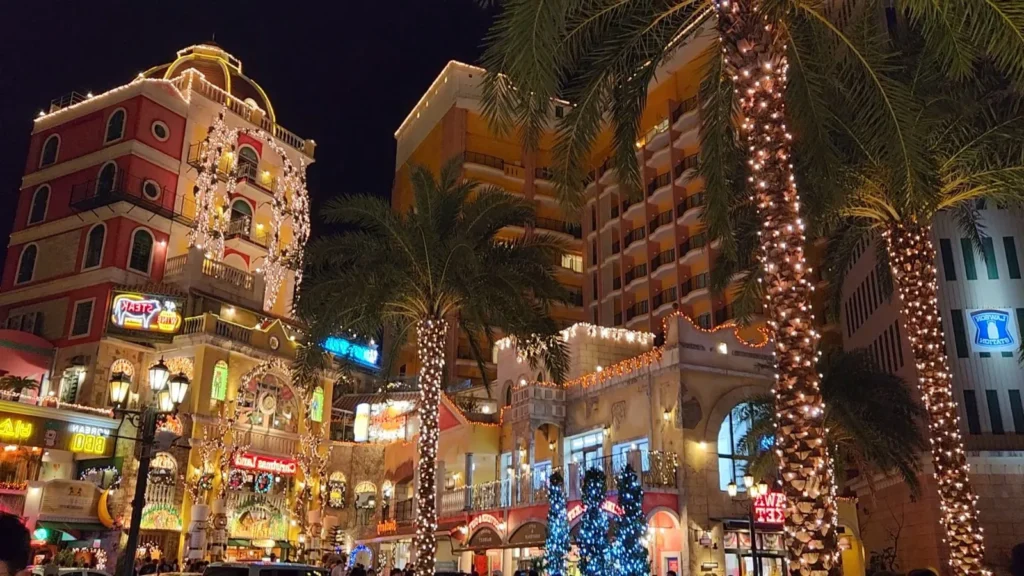 Palmiers illuminés et bâtiments de style européen brillant la nuit à l’American Village de Chatan, Okinawa, Japon.