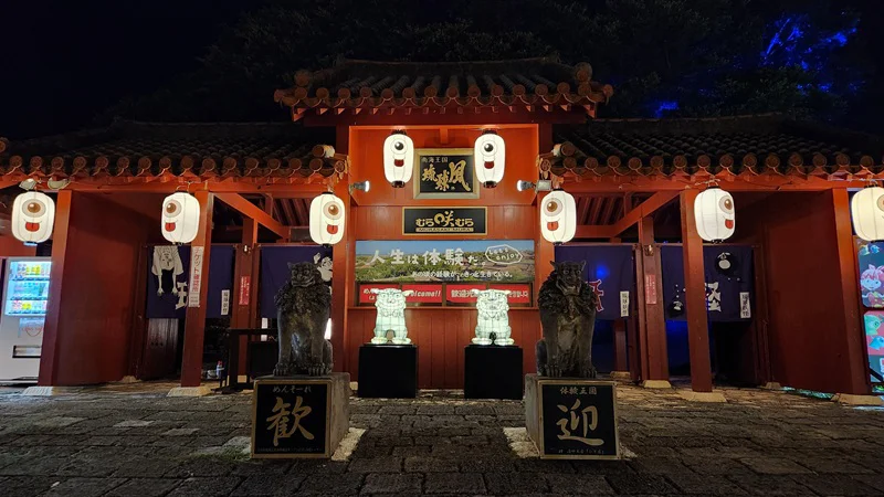 Illuminated entrance gate of Murasaki Mura with lanterns and shisa statues during the Ryukyu Yokai Festival