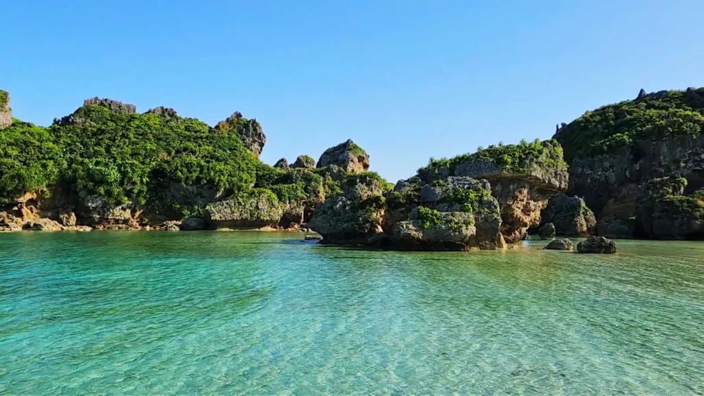 Transparent turquoise water with coral rocks along the coast of Hamahiga Island in Okinawa, Japan, under a bright blue sky.