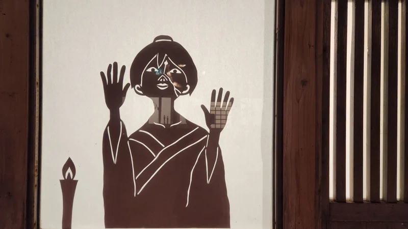 Shadow projection of a Jurimajimum yokai doll with cracked face on a shoji screen