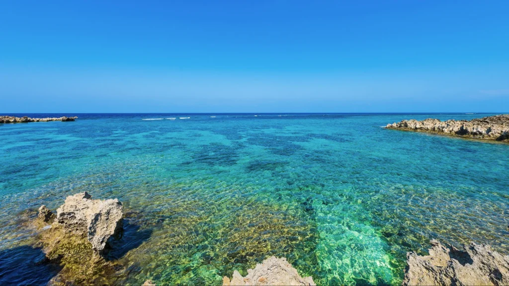 Transparent turquoise water with coral rocks along the coast of Hamahiga Island in Okinawa, Japan, under a bright blue sky.