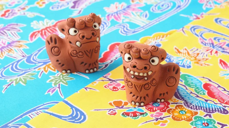Clay Shisa guardians displayed on colorful Okinawan Bingata fabric.