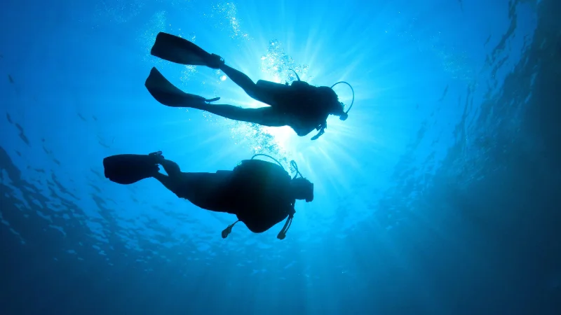 Two scuba divers underwater with sunlight shining through in Yomitan, Okinawa