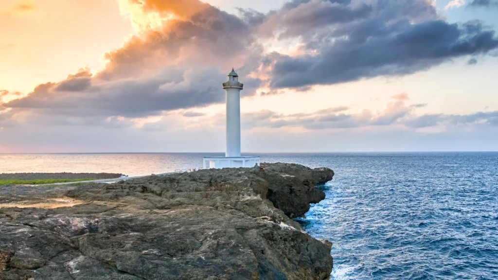 Phare blanc sur les falaises rocheuses du cap Zanpa dominant la mer de Chine orientale au coucher du soleil à Okinawa, Japon.