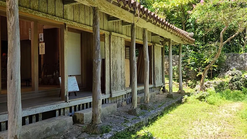 Wooden veranda and sliding doors of a traditional Okinawan house surrounded by greenery.