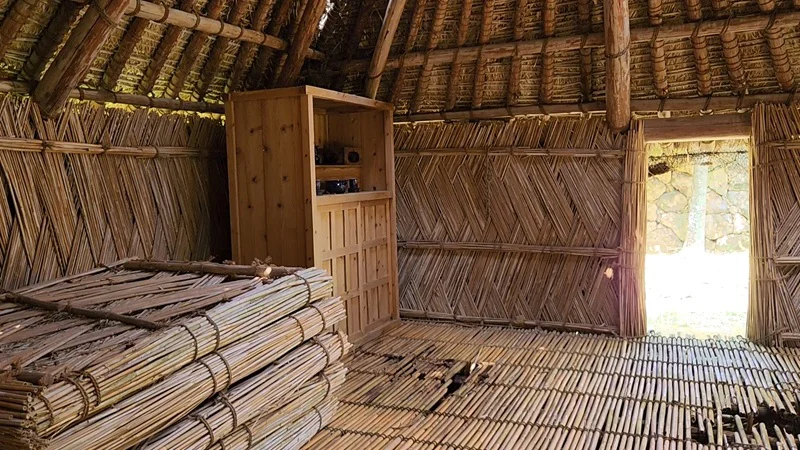 Inside a traditional Okinawan thatched hut with bamboo walls and wooden furniture.