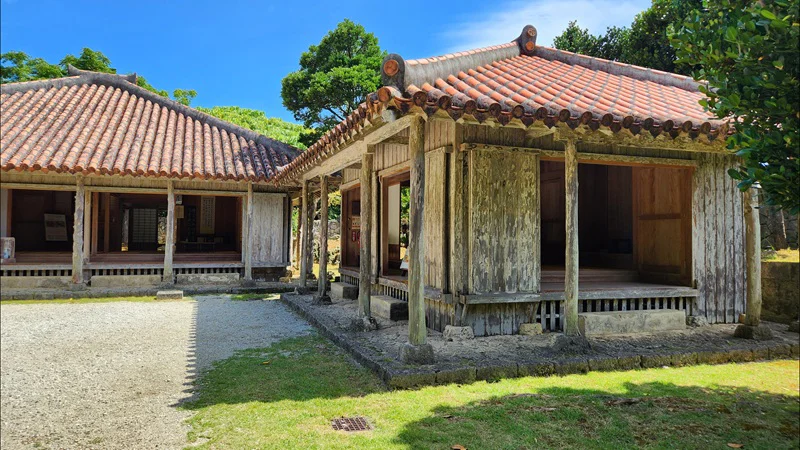 Traditional Okinawan wooden house with red-tiled roof at Jitūdē’s residence under a bright sky.