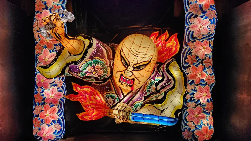 Illuminated warrior Mimichiri-bozu lantern with fierce expression and floral background at Ryukyu Lantern Festival