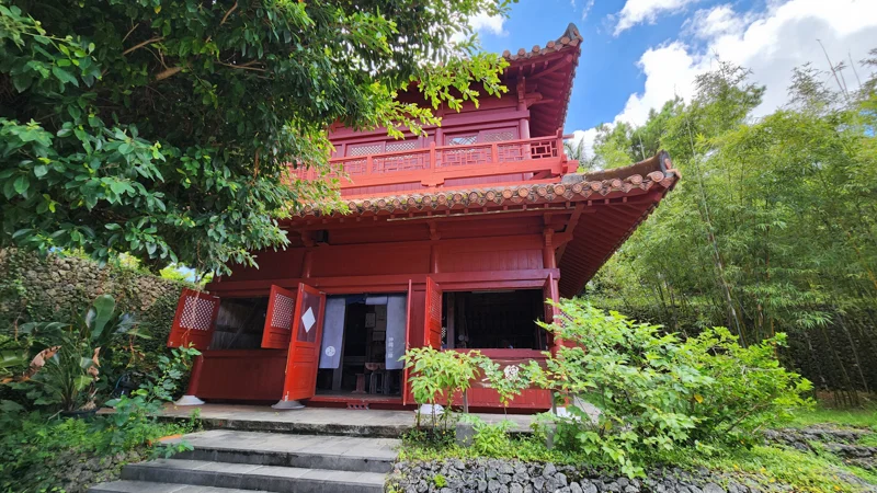 Two-story red Ryukyuan-style house surrounded by greenery at Murasaki Mura