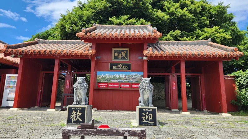 Traditional red gate of Murasaki Mura in Yomitan with shisa guardian statues