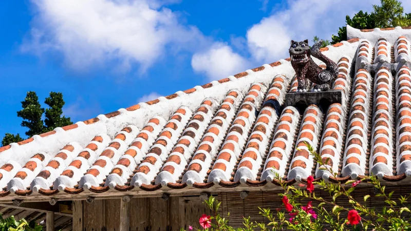 Shisa guardian statue on the red-tiled roof of a traditional Okinawan house.
