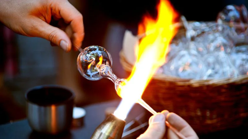 Artisan blowing molten glass in front of a flame