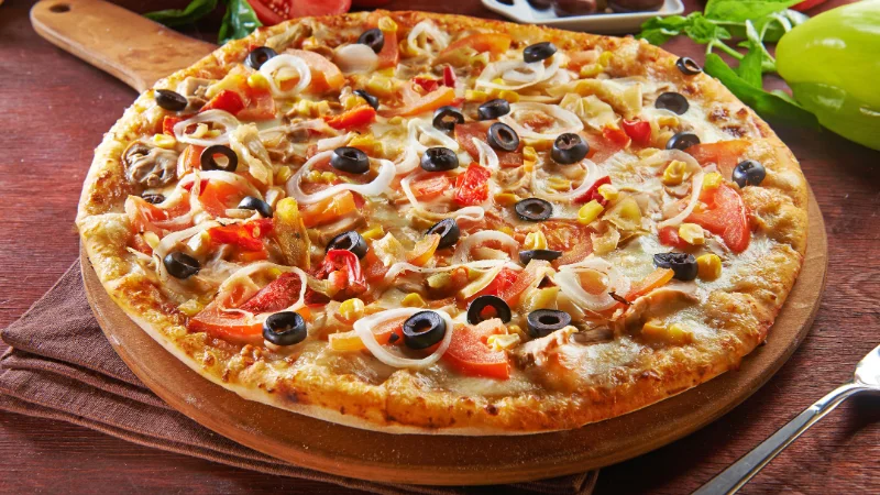 Freshly baked pizza with olives, tomatoes, and cheese at a restaurant in Yomitan