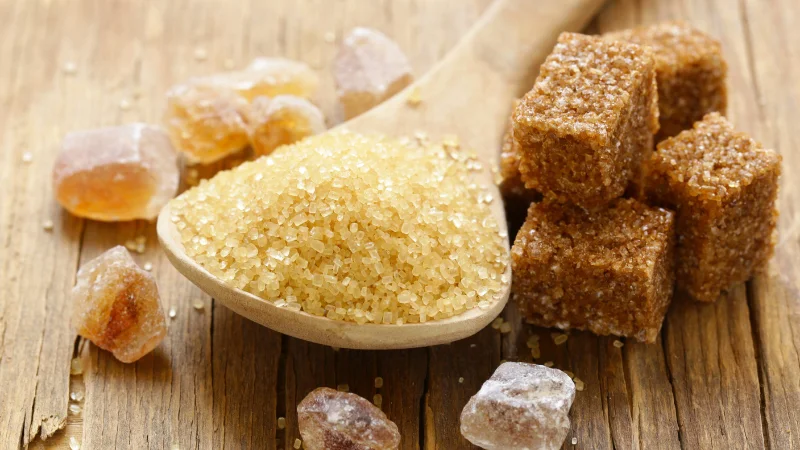 Okinawan brown sugar crystals and cubes on wooden table.