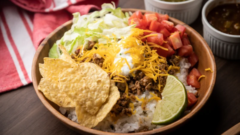 Okinawan taco rice bowl with ground beef, cheese, lettuce, tomato, and lime