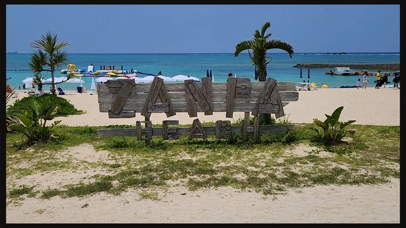 Wooden sign indicating Zanpa Beach in front of the turquoise sea