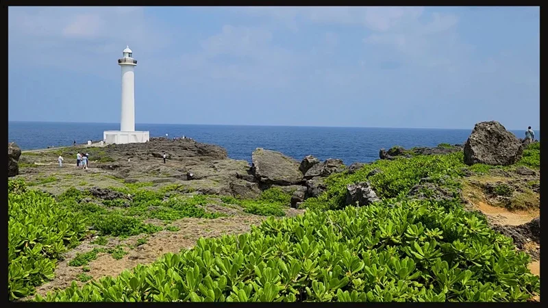 Walkers in front of the white lighthouse at Cape Zanpa