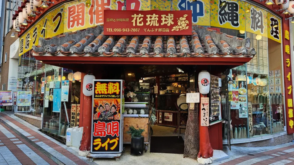 Front view of a traditional Okinawan restaurant on Kokusai Dori with red tiled roof, lanterns, and colorful signage in Naha, Okinawa.