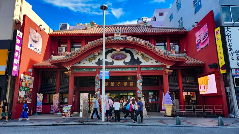 Front view of the Heiwa Dori market entrance in Naha, Okinawa, with people walking into the red traditional-style building.