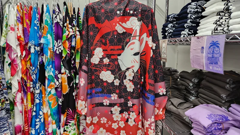 Red and black kimono jacket with a white kitsune mask design displayed among colorful clothing in a store.