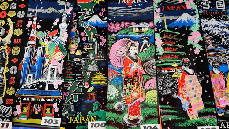 Decorative towels with Japanese landmarks, maps, geisha designs, and Mount Fuji patterns displayed in a shop.