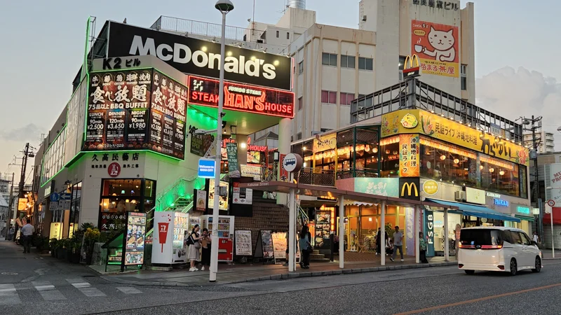 Street view of McDonald’s and Hans Steakhouse side by side on Kokusai Dori in Naha, with illuminated signs at dusk.
