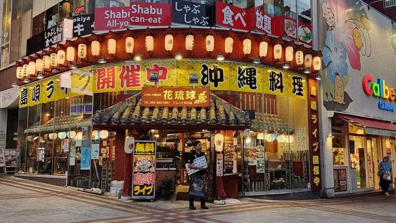 Exterior of a traditional Okinawan restaurant on Kokusai Dori with lanterns, banners, and red tiled roof.