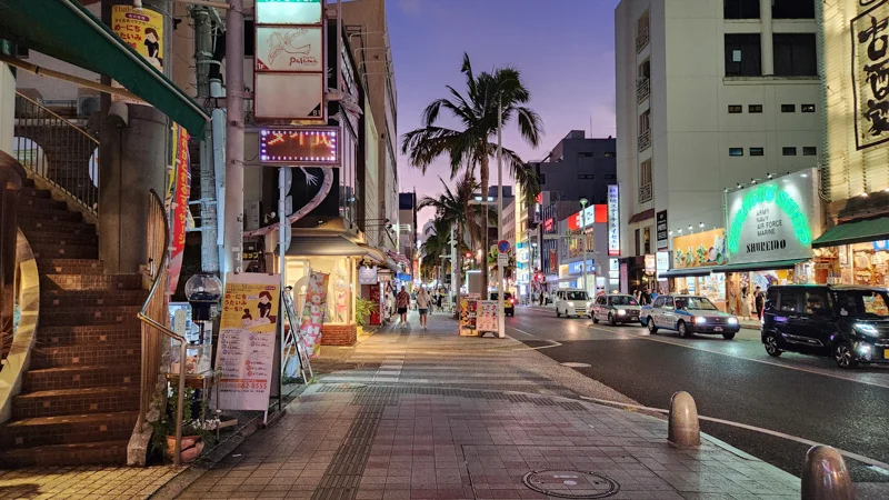 Busy evening view of Kokusai Dori with cars, palm trees, and illuminated shops in Naha, Okinawa.