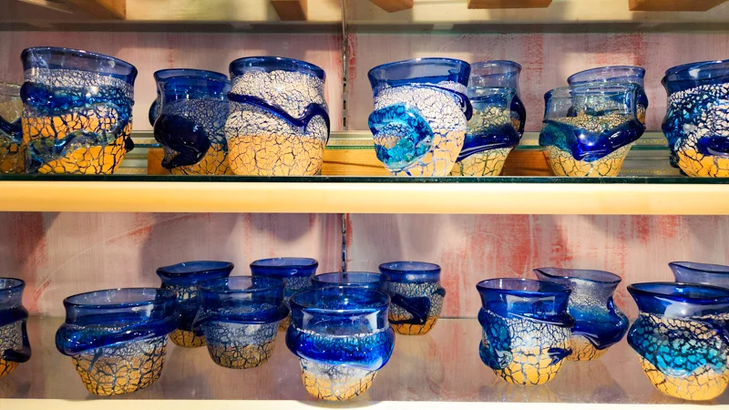Shelves filled with handcrafted blue and gold Ryukyu glass cups displayed in an Okinawan shop.
