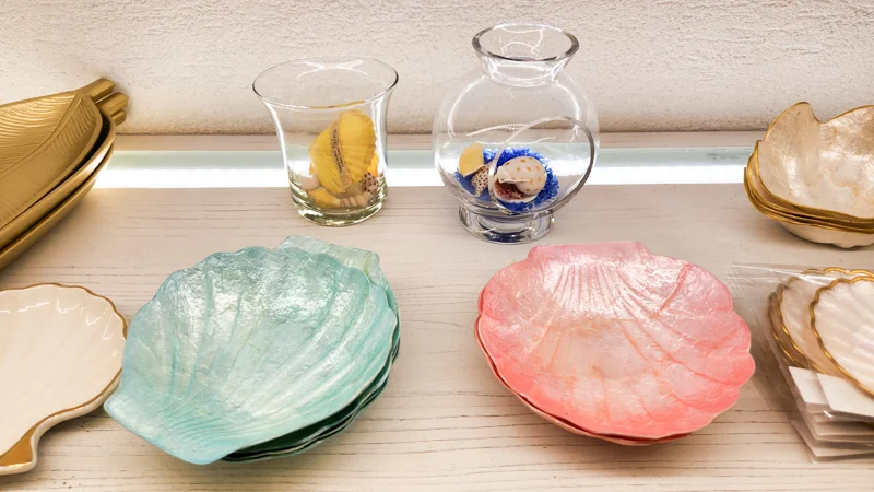 Display of pastel seashell plates and small ocean-themed glass ornaments in an Okinawan souvenir shop.