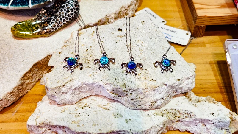 Silver sea turtle necklaces with blue glass pendants displayed on coral-like stones in a shop.
