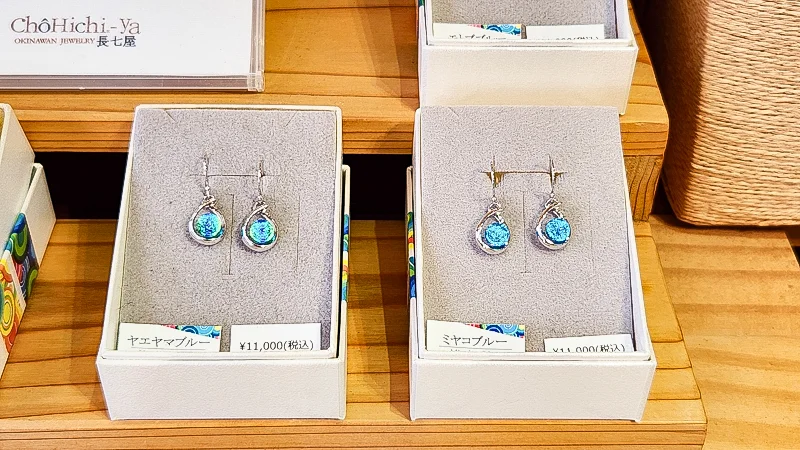 Elegant blue glass earrings displayed in white jewelry boxes inside an Okinawan shop.