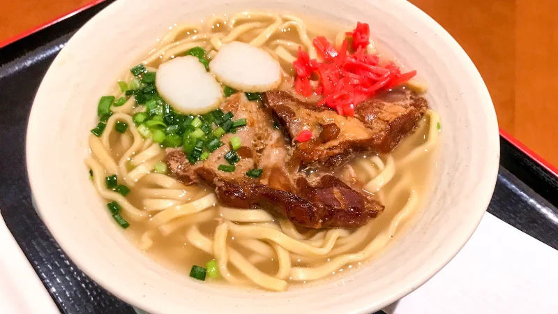 Bowl of Okinawa soba with pork, fish cake, ginger, and green onions