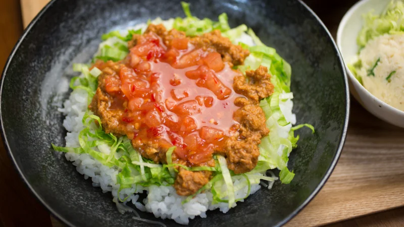 Bowl of Okinawa taco rice with seasoned meat, lettuce, and fresh salsa