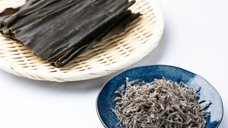 Dried kombu sheets and a bowl of shredded shio kombu on white background