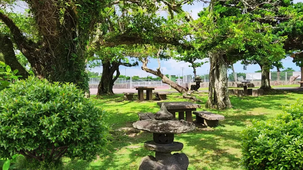 Stone lanterns and wooden picnic tables under banyan trees in a quiet park in Okinawa, Japan