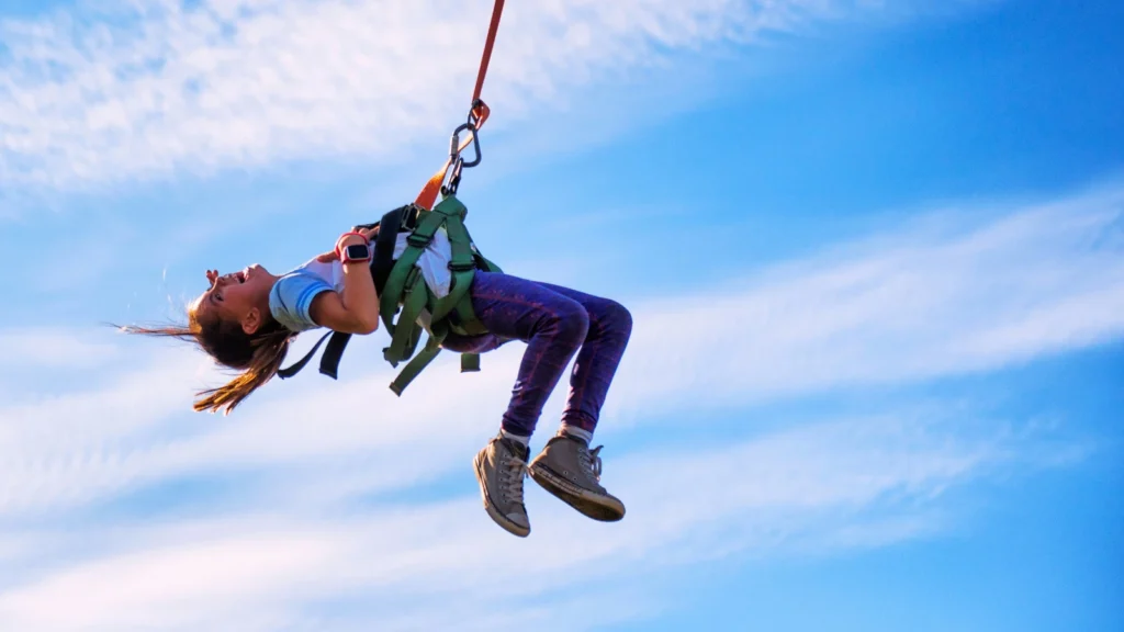 Child wearing a safety harness enjoying a zipline ride at a theme park in Japan under a blue sky
