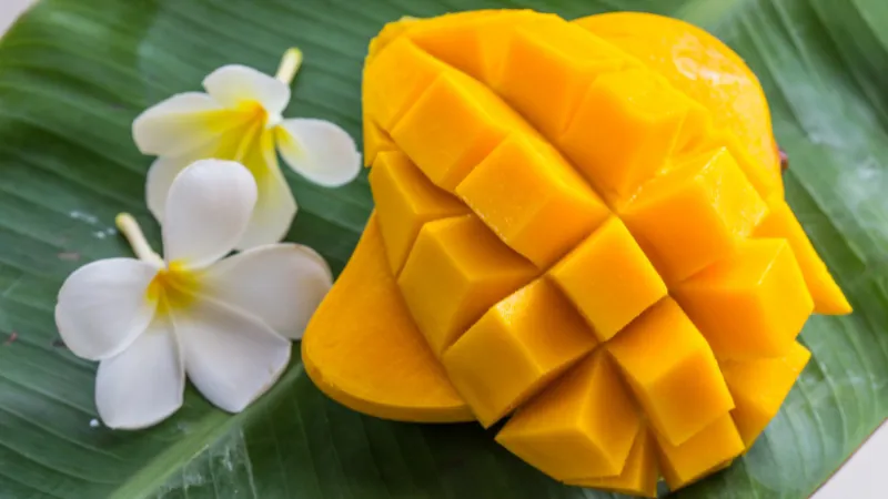 Sliced Okinawan mango cut into cubes on a banana leaf with two white tropical flowers beside it.