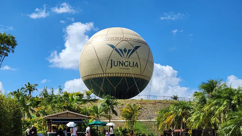 Large Junglia Okinawa hot air balloon rising above tropical plants under a bright blue sky