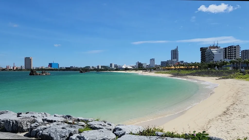 Curved beach with green water and city buildings at Sunset Beach Chatan Okinawa