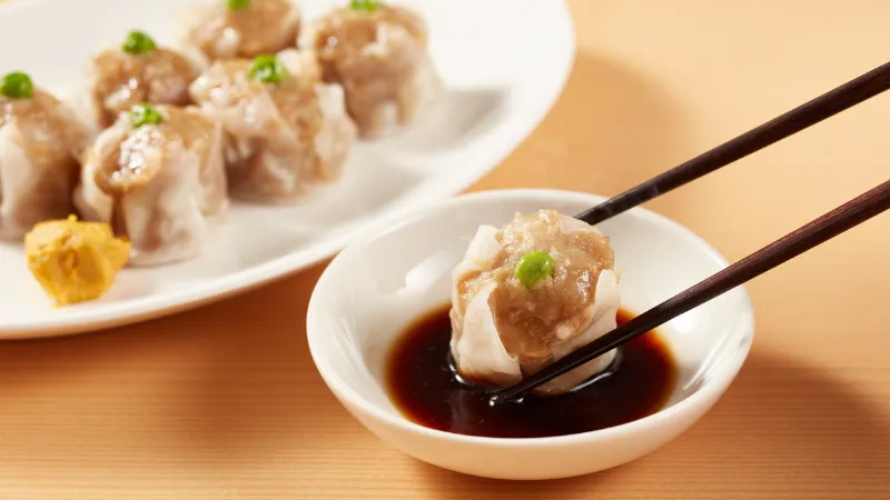 Steamed Japanese dumpling held with chopsticks over soy sauce