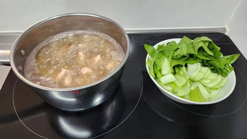 コンロの上で、野菜入りのだしの中で鶏肉を煮ている調理中の鶏スープ。
