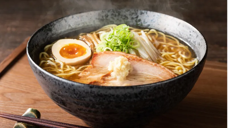 Bowl of Japanese ramen with noodles, sliced pork, soft boiled egg, and green onions