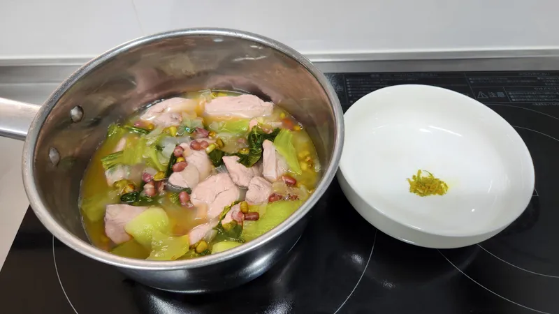 野菜と豆と一緒に鍋で煮ている鶏スープ。