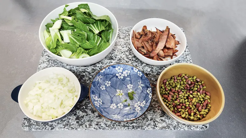 鶏スープを作るための、刻んだチンゲン菜、鰹節、角切りの玉ねぎ、ミックス豆を入れたボウル。
